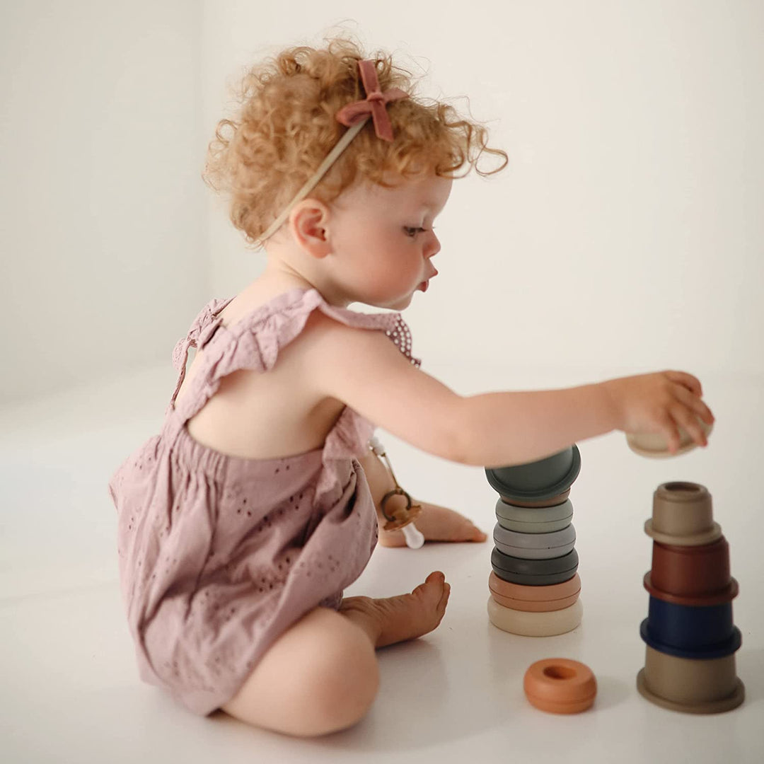 A little girl plays with Mushie stacking cups, as sold by Mabel & Fox 