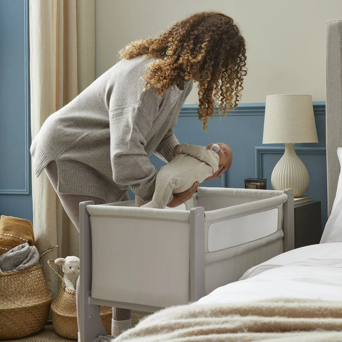 Women placing baby into a bedside crib.