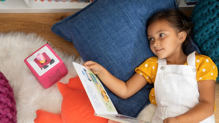 Girl reading a book while listening to a Tonies audio player
