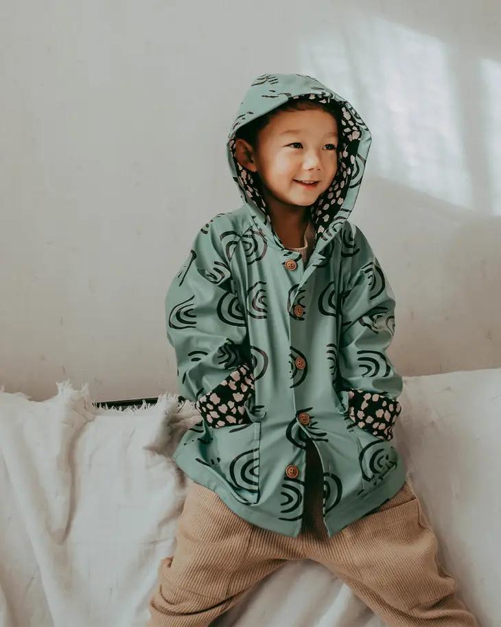 Turtledove London create unisex organic clothes for 0-5year olds. The image features a young child wearing a rainbow raincoat. 