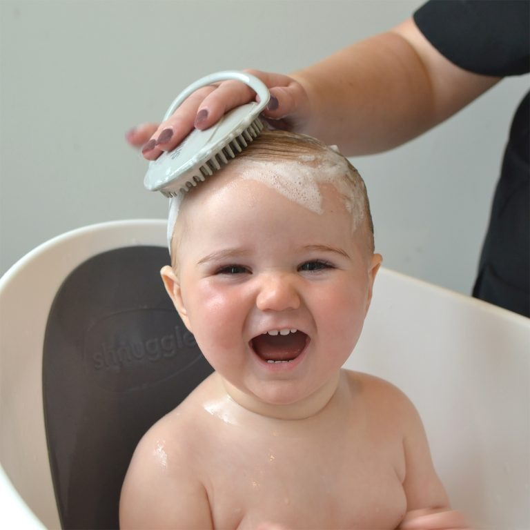 Shnuggle develops products to make life easier and safer for growing families, sold by Mabel & Fox. Image features their grey baby bath brush.