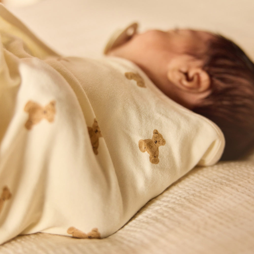 Baby wrapped in a blanket with bear patterns lying on a bed.