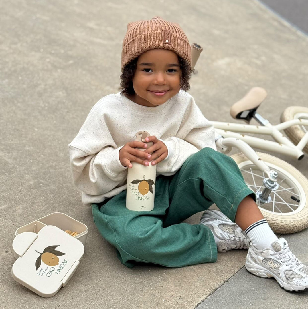 Child sitting on a sidewalk holding a bottle, with a bicycle in the background