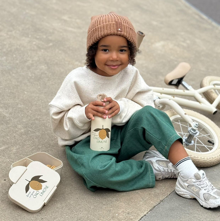 Child sitting on a sidewalk holding a bottle, with a bicycle in the background