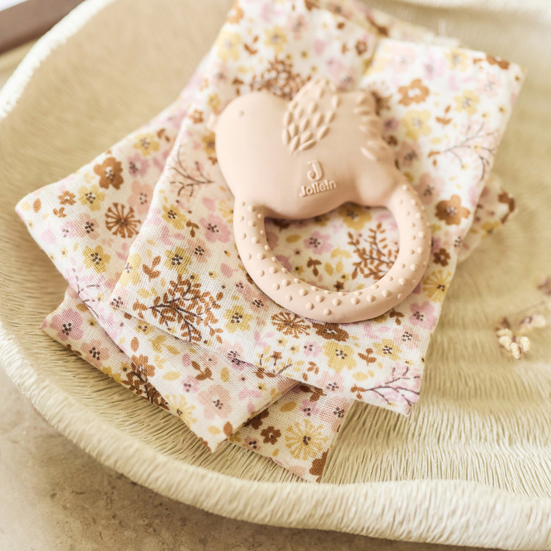 Floral-patterned baby blanket with teething ring on a beige plate