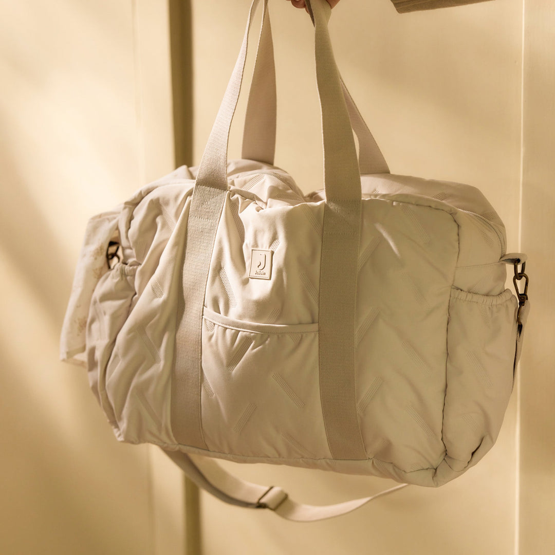 Beige duffel bag held by a hand against a beige background
