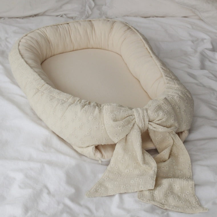 Beige baby nest with bow on a white textured surface