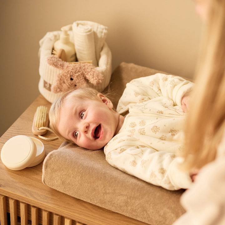 Baby wrapped in a white blanket on a changing table with a basket of items in the background.