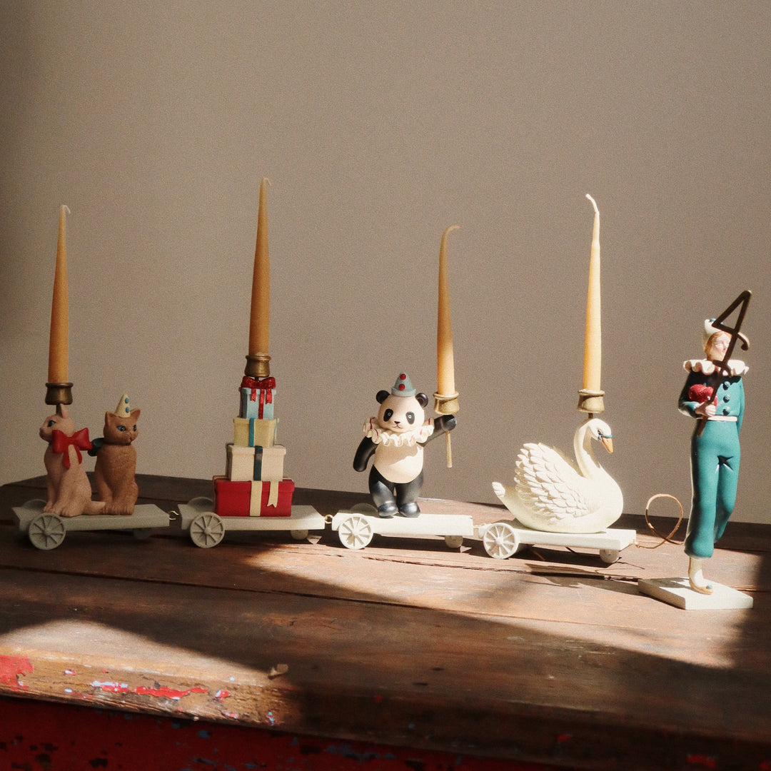 Decorative items including candles, figurines, and a swan on a wooden surface with a neutral background.