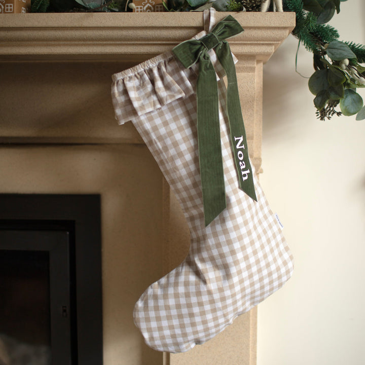 Checkered Christmas stocking with a green ribbon and 'Noah' embroidery on a fireplace mantel.