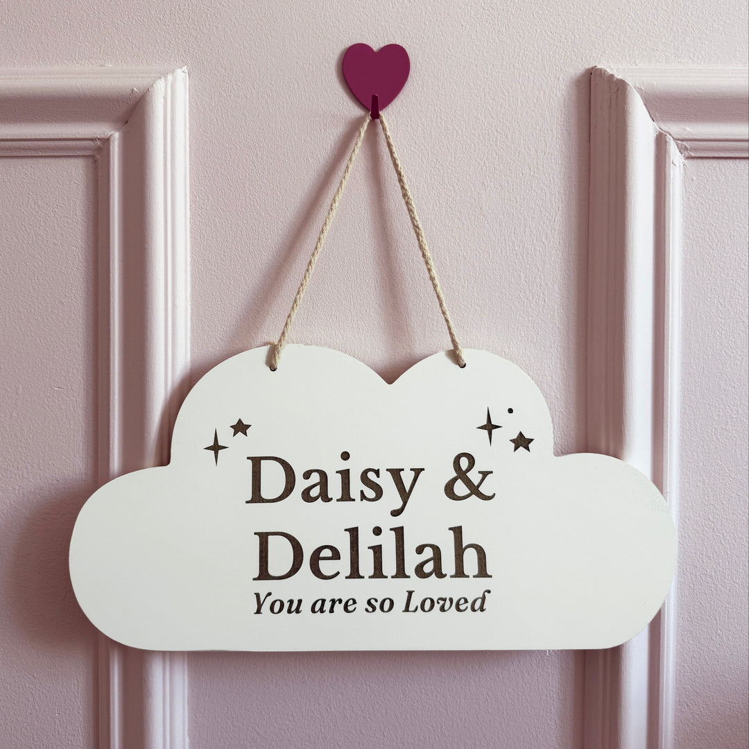 Decorative cloud-shaped sign with 'Daisy & Delilah You are so Loved' text on a pink wall.
